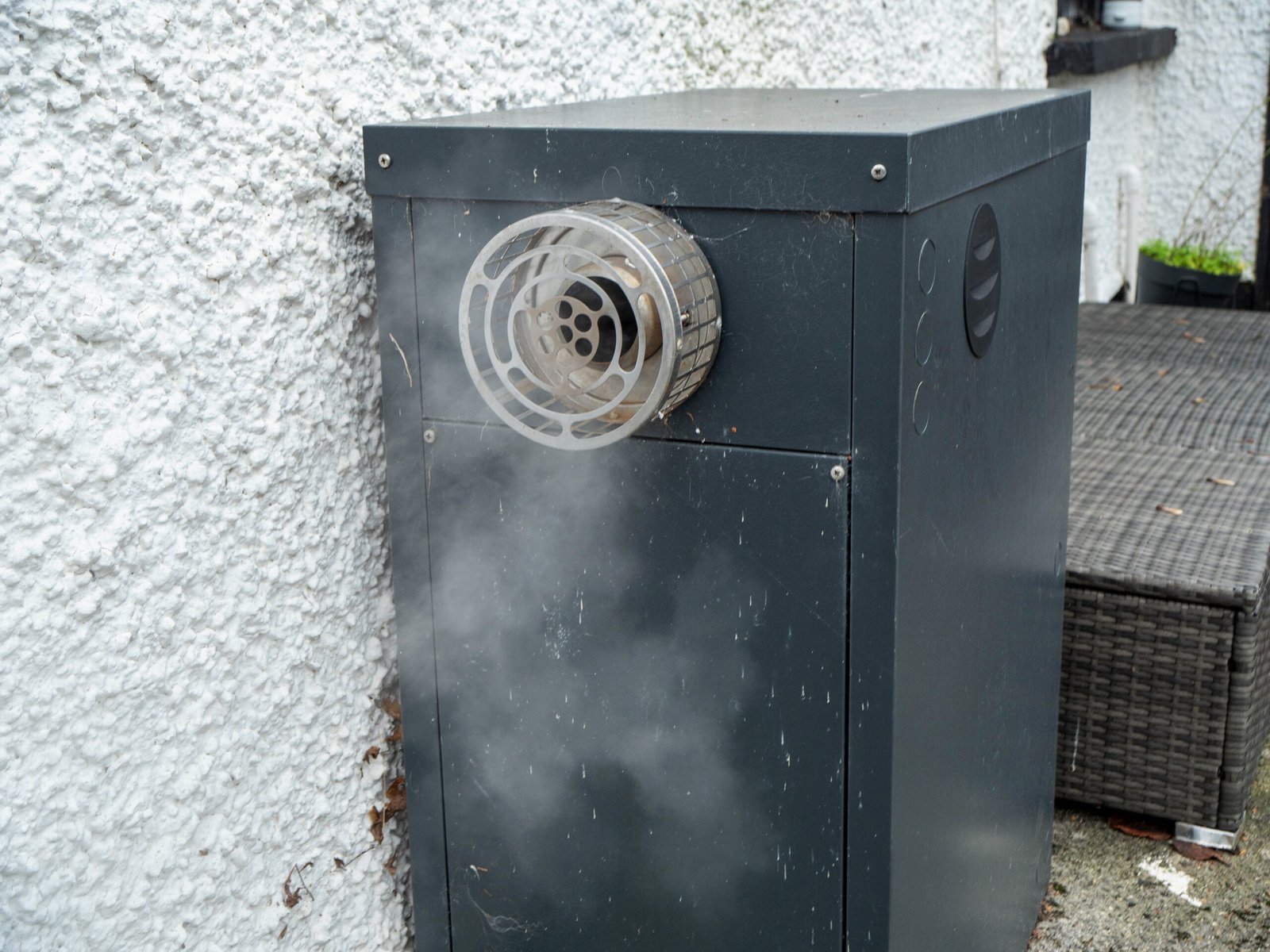Old heating oil heater outside building at work with smoke coming out from small chimney. Country house. Home looks old with white walls and located in a remote country side.